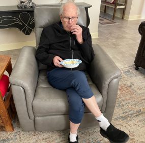 grandfather sitting on a gray sofa chair eating popcorn